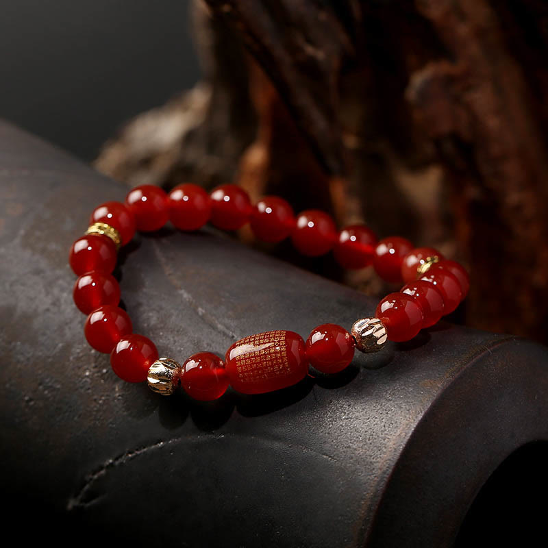 Red Green Agate Buddhist Sutras Calm Bracelet – low angle on dark ceramic prop with blurred wood backdrop, warm studio light,