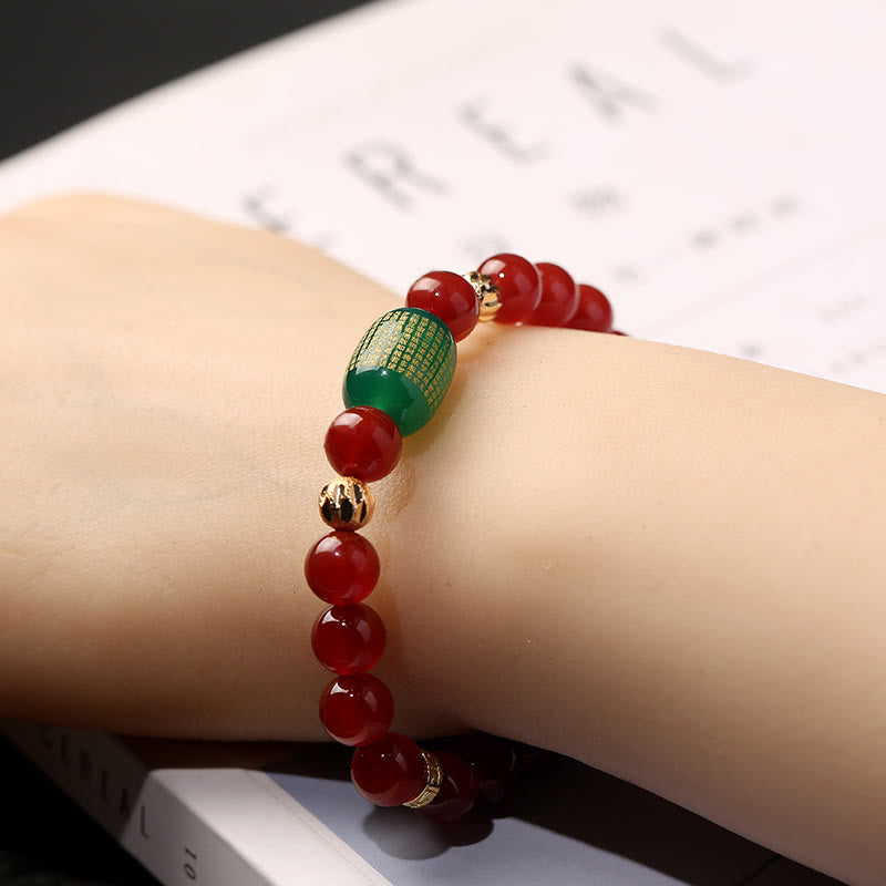 Red Green Agate Buddhist Sutras Calm Bracelet – worn on wrist over open book, green mantra bead and gold spacers visible, min