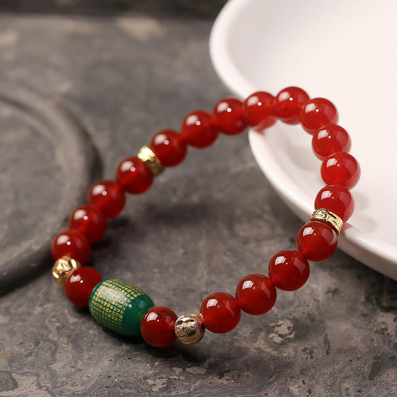 Red Green Agate Buddhist Sutras Calm Bracelet – polished carnelian beads and gold sutra bead on white dish over stone, spirit