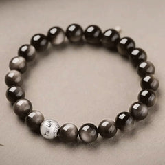 Silver Sheen Obsidian Bracelet – top down circular arrangement on beige fabric with engraved silver bead, grounding