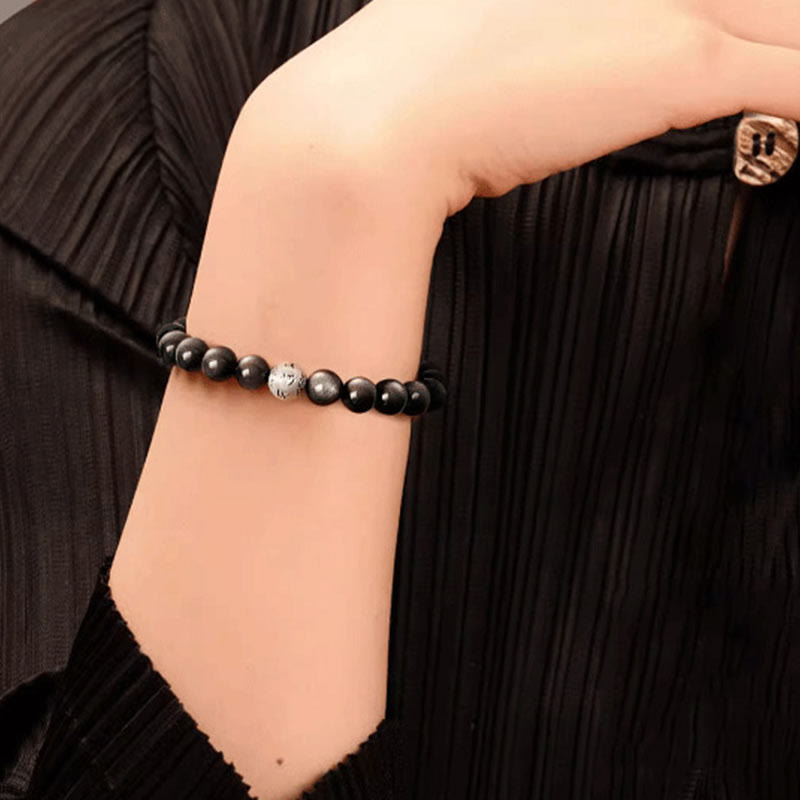 Silver Sheen Obsidian Bracelet – worn on wrist over black ribbed sleeve showing silvery shimmer, protection grounding