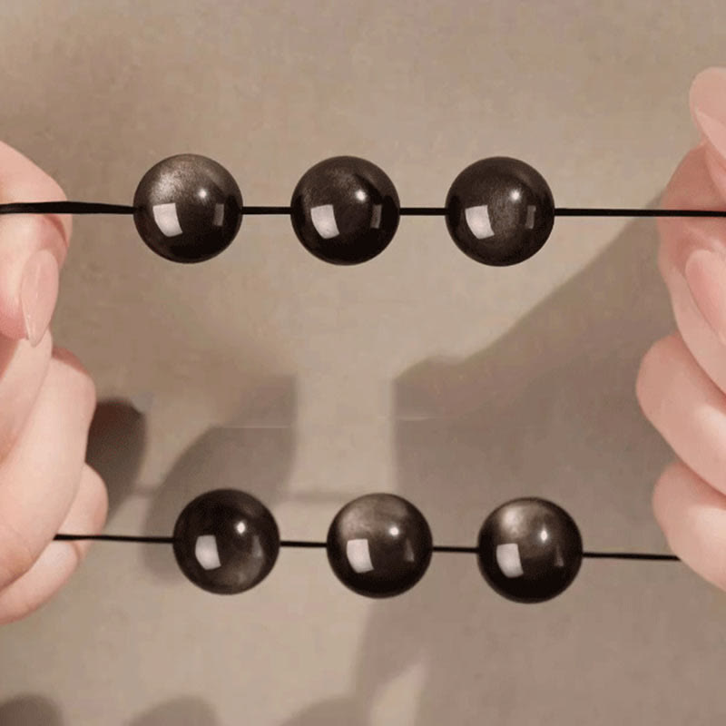 Silver Sheen Obsidian Bracelet – stretched between hands with mirror reflection on glossy surface, grounding