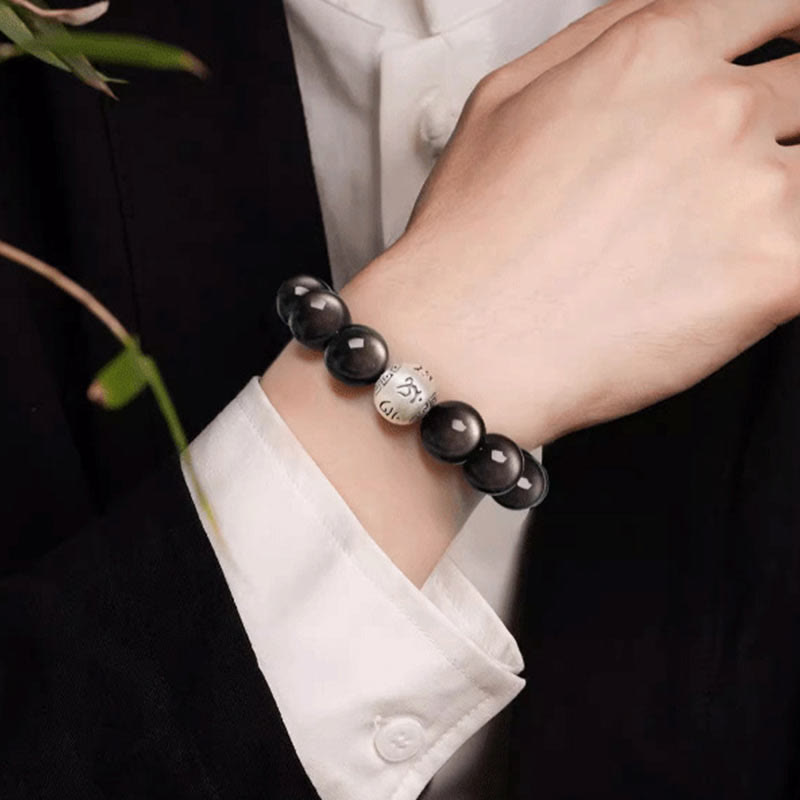 Silver Sheen Obsidian Bracelet – worn on wrist with white shirt cuff against dark backdrop and foliage, grounding