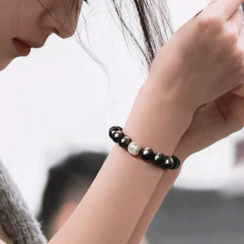 Silver Sheen Obsidian Bracelet – on wrist near face with gray knit sweater in contemplative pose, grounding protection