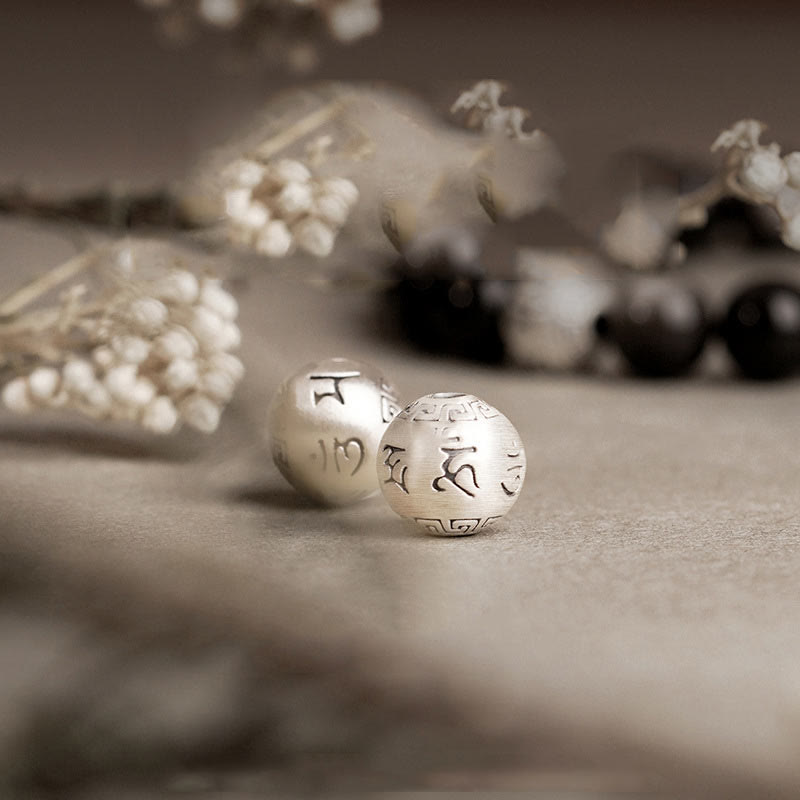 Silver Sheen Obsidian Bracelet – macro of engraved silver mantra bead on stone with dried flowers, spiritual grounding
