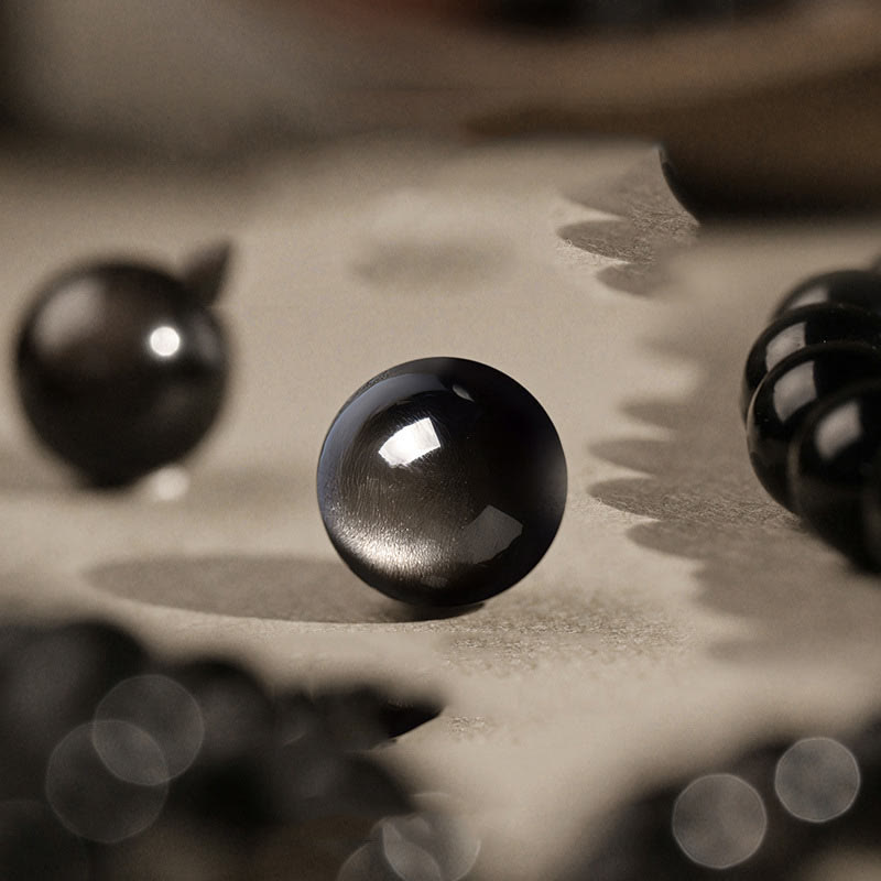 Silver Sheen Obsidian Bracelet – close up of polished black bead showing silver sheen flash on paper, grounding energy