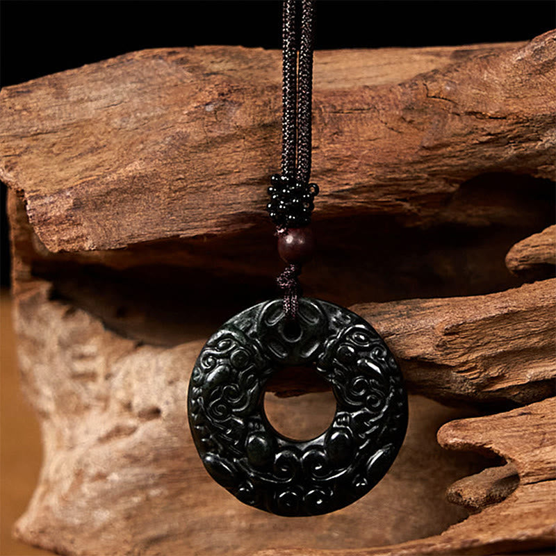Black-green jade pendant hanging against natural driftwood background