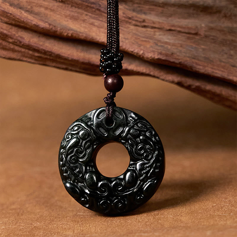 Black-green jade PiXiu peace buckle pendant on cord against brown wood
