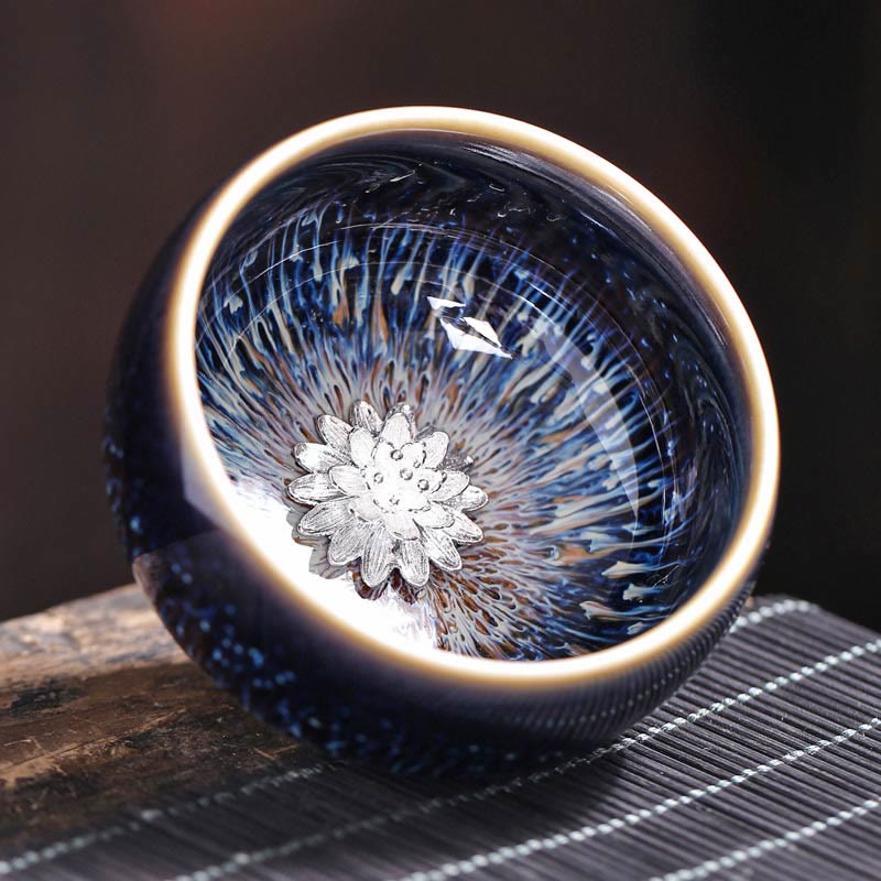 Jianzhan 12 Cup Set - cup with silver lotus flower center, tilted on wood, tenmoku glaze