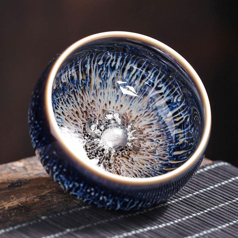 Jianzhan 12 Cup Set - cup with silver toad ornament, three-quarter view, blue iridescent glaze