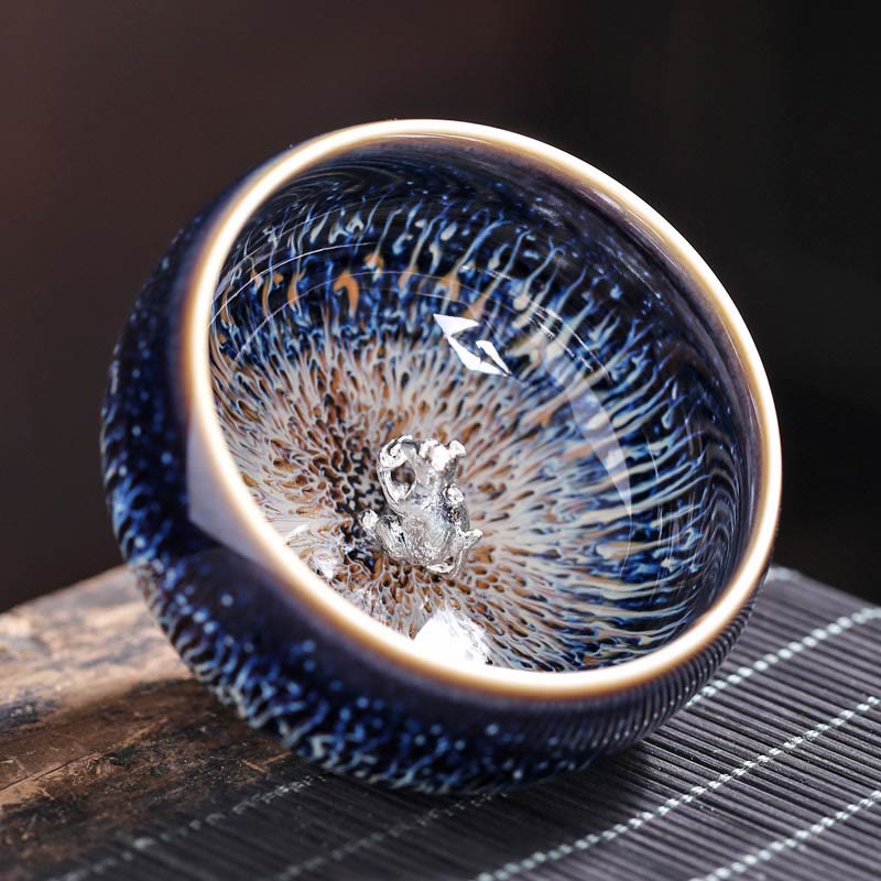 Jianzhan 12 Cup Set - cup with silver animal ornament, three-quarter view on bamboo mat