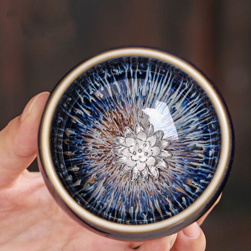 Jianzhan 12 Cup Set - top-down cup with silver lotus medallion in hand, starburst glaze