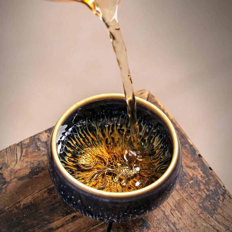 Jianzhan 12 Cup Set - amber tea poured into black cup with gold ornament on wood
