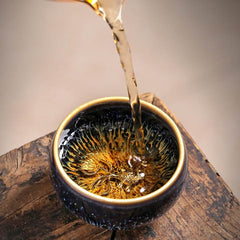 Jianzhan 12 Cup Set - amber tea poured into black cup with gold ornament on wood