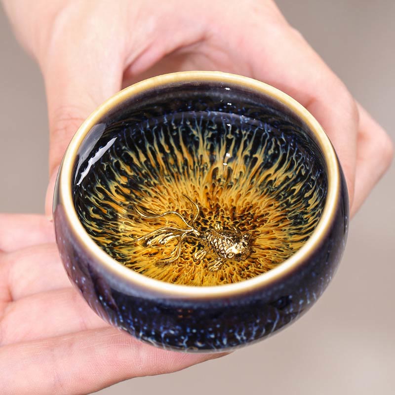 Jianzhan 12 Cup Set - golden koi cup held in hands, starry blue hare's fur glaze