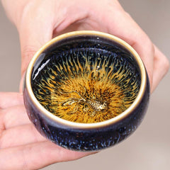 Jianzhan 12 Cup Set - golden koi cup held in hands, starry blue hare's fur glaze
