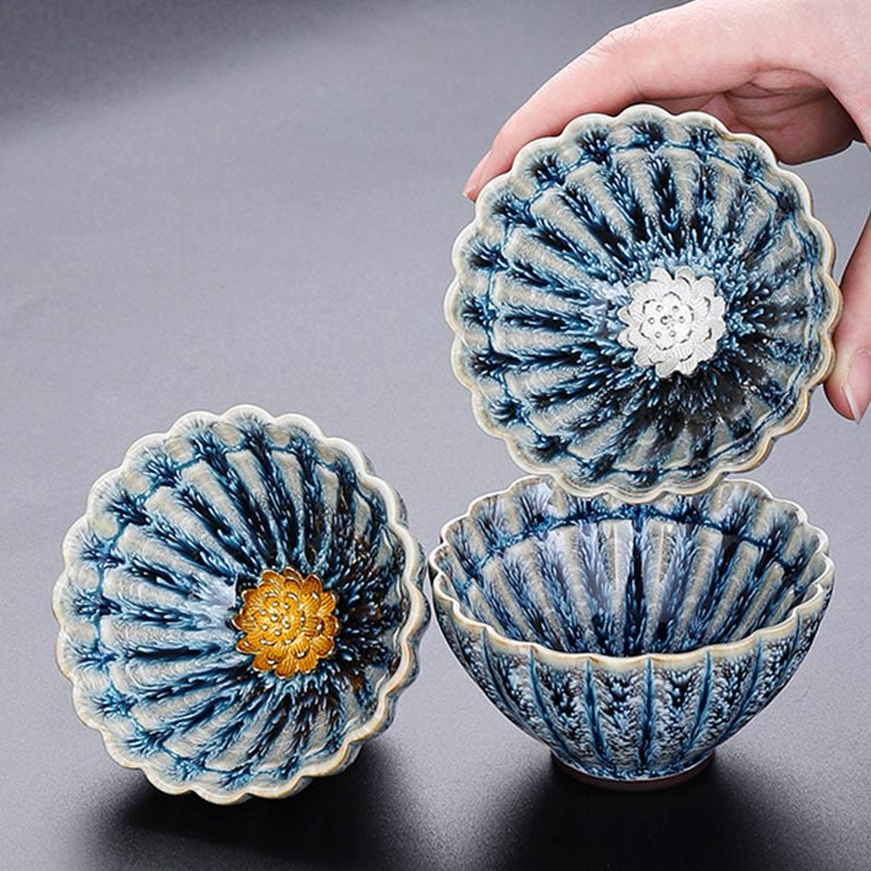 Three Jianzhan Lotus Ceramic Tea Cups with gold and silver centers, hand holding one, artisan