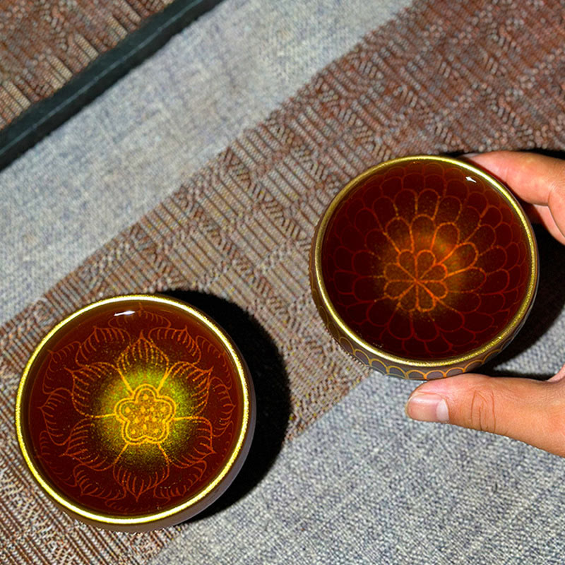 Lotus Flower Ceramic Tea Cup – gold floral patterns visible through amber tea, hand holding, Jianzhan