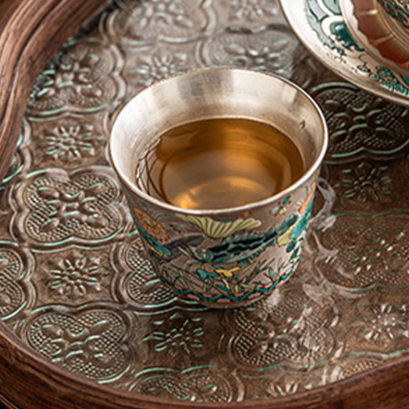 Fish Lotus Tea Cup – filled with amber tea on embossed silver tray, elevated angle, artisan teacup