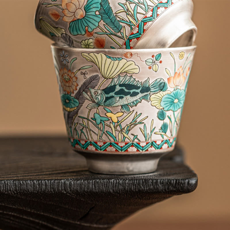 Fish Lotus Tea Cup – nested pair on dark hardwood, low angle highlighting enamel fish detail, artisan teacup