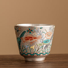 Fish Lotus Tea Cup – silver metallic body with koi and lotus enamel, studio side view, artisan teacup