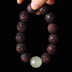 Tibetan Rosewood Engraved Pixiu Warmth Healing Bracelet – hand held vertically with glowing jade bead, spiritual protection bracelet