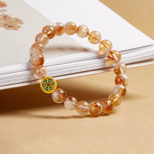 999 Sterling Silver Citrine Om Mani Padme Hum Bracelet – draped over book with botanical illustration, showing warm amber stone translucency and mandala bead detail