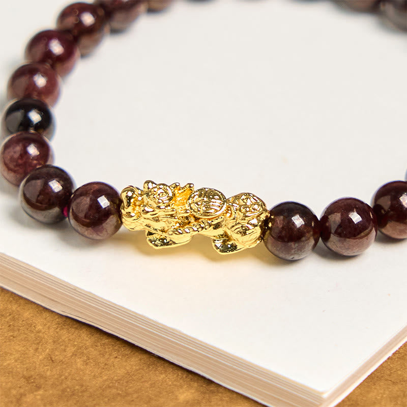 Natural Garnet Pixiu Protection Bracelet – close-up of ornate gold Pixiu charm between dark garnet beads, feng shui wealth protection detail view