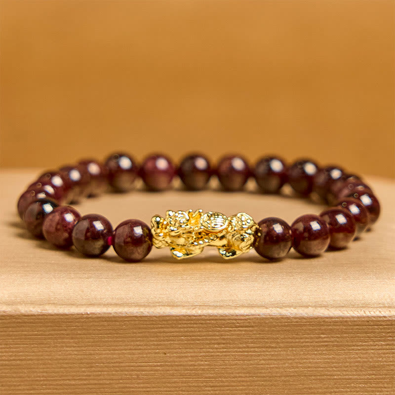 Natural Garnet Pixiu Protection Bracelet – front view with amber background, dark red garnet beads with ornate gold Pixiu centerpiece, good luck
