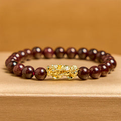 Natural Garnet Pixiu Protection Bracelet – front view with amber background, dark red garnet beads with ornate gold Pixiu centerpiece, good luck