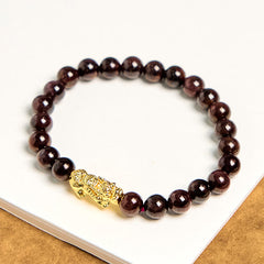 Natural Garnet Pixiu Protection Bracelet – flat lay on white surface showing full circle of dark red garnet beads with gold Pixiu charm, feng shui