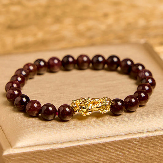 Natural Garnet Pixiu Protection Bracelet – front view on gold box showing dark red garnet beads with large gold Pixiu charm center, feng shui wealth