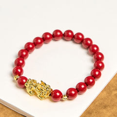 Cinnabar Pixiu Calm Bracelet – flat lay on white surface showing full circle of red cinnabar beads with gold Pixiu charm center, wealth