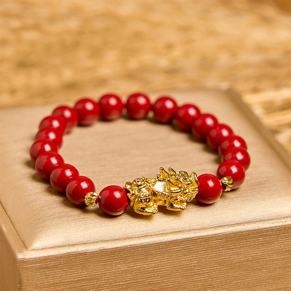 Cinnabar Pixiu Calm Bracelet – front view on gold box, single strand red cinnabar beads with large gold Pixiu charm center, feng shui
