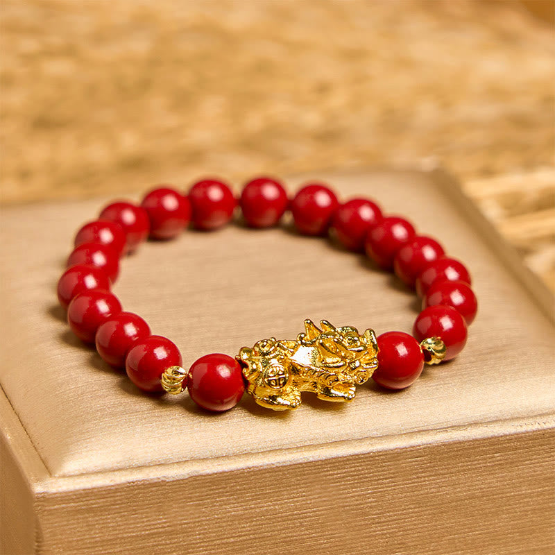 Cinnabar Pixiu Calm Bracelet – front view on gold box, single strand red cinnabar beads with large gold Pixiu charm center, feng shui
