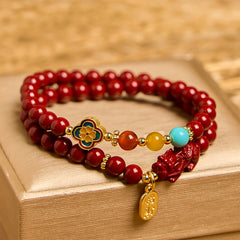 Cinnabar Pixiu Fu Bracelet – front view on gold box showing double wrap red cinnabar beads with enamel flower and Pixiu charm, feng shui