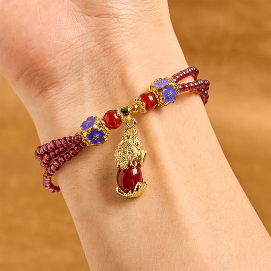 Garnet Pixiu Flower Bracelet – wrist view showing triple strand garnet with blue enamel flowers and gold Pixiu pendant, feng shui wealth charm