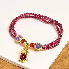 Garnet Pixiu Flower Bracelet – flat lay on white surface showing full triple strand design with blue enamel flowers and gold Pixiu, protection luck