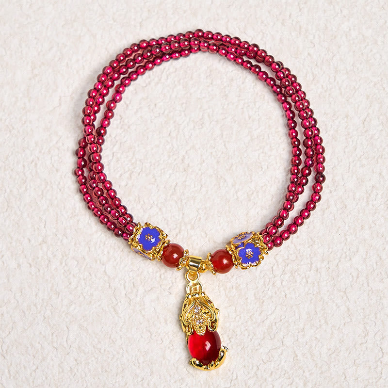 Garnet Pixiu Flower Bracelet – full circle view on textured white background with triple strand garnet, blue flowers and gold Pixiu, wealth protection