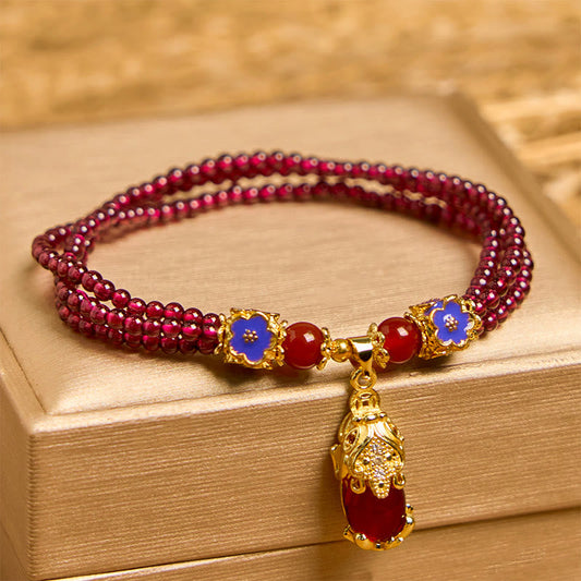 Garnet Pixiu Flower Bracelet – front view on gold box, triple strand garnet beads with blue enamel flowers and gold Pixiu, feng shui wealth