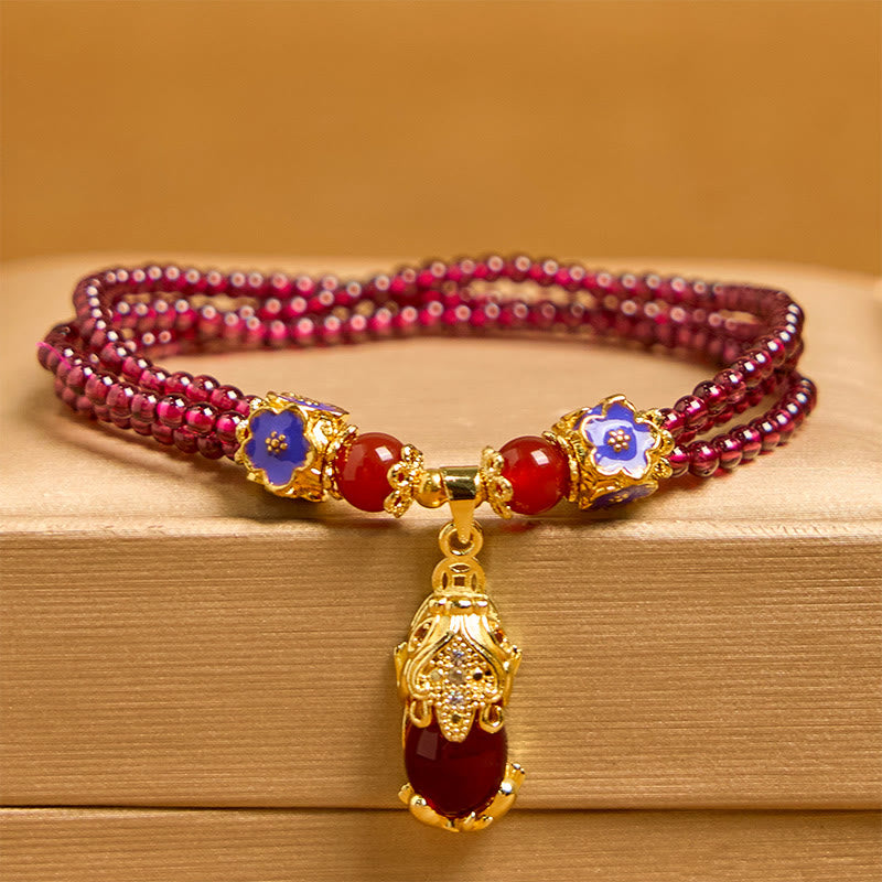 Garnet Pixiu Flower Bracelet – front view with amber background, triple strand garnet, blue enamel flowers and gold Pixiu, good luck