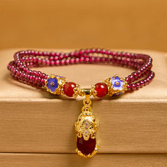 Garnet Pixiu Flower Bracelet – front view with amber background, triple strand garnet, blue enamel flowers and gold Pixiu, good luck