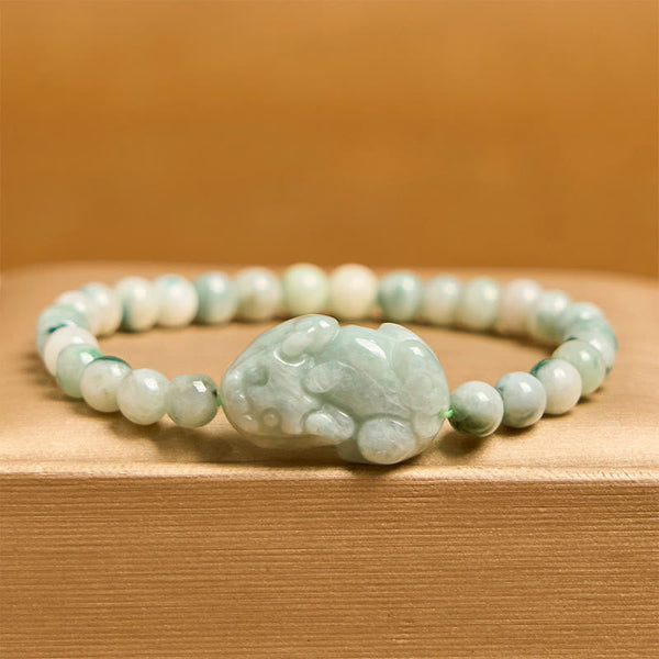 Natural Green Jade Pixiu Carved Luck Bead Bracelet – side view of jade Pixiu bracelet on wood surface with orange backdrop, good luck accessory