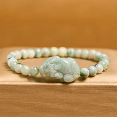 Natural Green Jade Pixiu Carved Luck Bead Bracelet – side view of jade Pixiu bracelet on wood surface with orange backdrop, good luck accessory