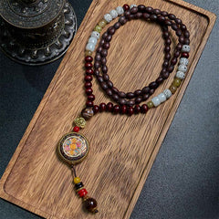 Tibetan Om Mani Padme Hum Necklace – Top-down view on wooden tray, enamel flower medallion pendant, red beads