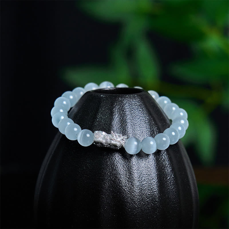 Cat's Eye 990 Sterling Silver Pixiu Positive Energy Bracelet – white bracelet draped on black ceramic vase with green foliage background, lucky charm