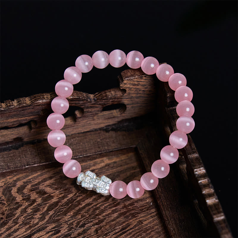Cat's Eye 990 Sterling Silver Pixiu Positive Energy Bracelet – pink bracelet on dark carved wood surface with black background, abundance charm