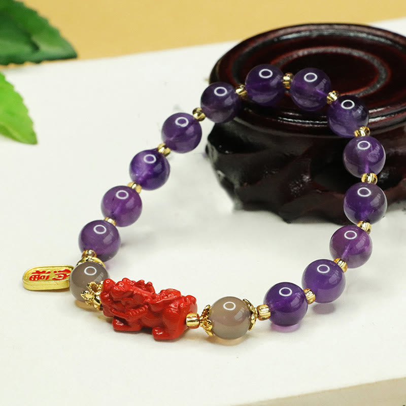 Amethyst Cinnabar Pi Xiu Fu Character Balance Bracelet – angled view on carved wooden base showing amethyst and gray beads, feng shui bracelet