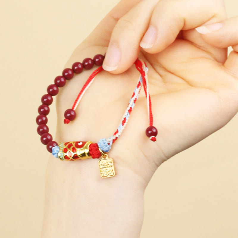 Cinnabar Koi Fish Blessing Bracelet – worn on model wrist, burgundy beads, gold fish charm, adjustable braided cord, cream bg