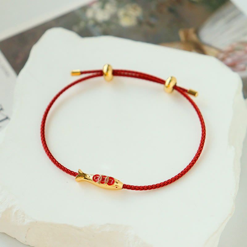 Brass Koi Fish Red String Bracelet – on white stone surface, gold koi charm red enamel scales, adjustable prosperity cord